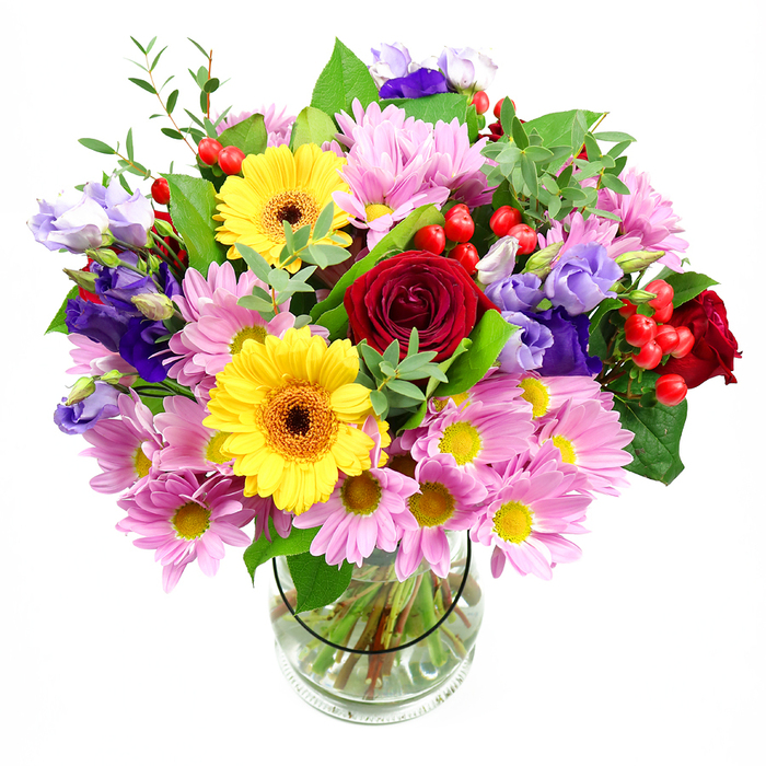 This photograph captures a vibrant mixed-colour bouquet displayed in a simple clear glass vase, the whole arrangement standing out against a pure white backdrop so every bloom can be imagined in vivid detail. At the heart of the design, rich red roses open in velvety layers, their deep tones adding emotional depth and a classic, romantic touch. Sharing the focus are two bold yellow gerbera daisies, their broad petals radiating around dark brown-orange centres, giving the bouquet a bright, sunlit feel reminiscent of a clear afternoon near Uxbridge station. Surrounding these centrepieces is a generous collar of soft pink daisies and chrysanthemums, with many delicate petals circling small yellow centres. Together they create a cloud of gentle colour and texture that softens the stronger reds and yellows. Between these pastel blooms, elegant purple and lavender lisianthus stretch upwards and outwards, their bell-like flowers contributing cooler notes and graceful curves, like ripples on the Grand Union Canal. Nestled among the flowers, clusters of glossy red hypericum berries add rounded shapes and a slightly playful, contemporary dimension. The greens are abundant and varied: broad, dark leaves provide a solid backdrop, while slender, lighter green stems and sprigs weave in and out, lending freshness and movement as if the bouquet had just been gathered from fields near Hillingdon. Through the transparent vase, the neatly arranged stems can be seen fanning into clear water, reflecting the care and expertise of an experienced florist. The overall impression is of warmth, joy, and easy celebration, a bouquet that would feel perfectly placed on a kitchen table in a Uxbridge family home or delivered as a thoughtful surprise to a colleague in an office near The Pavilions shopping centre.